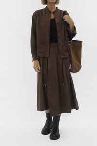 Person wearing a brown outfit with a matching jacket, skirt, and bag on a white background