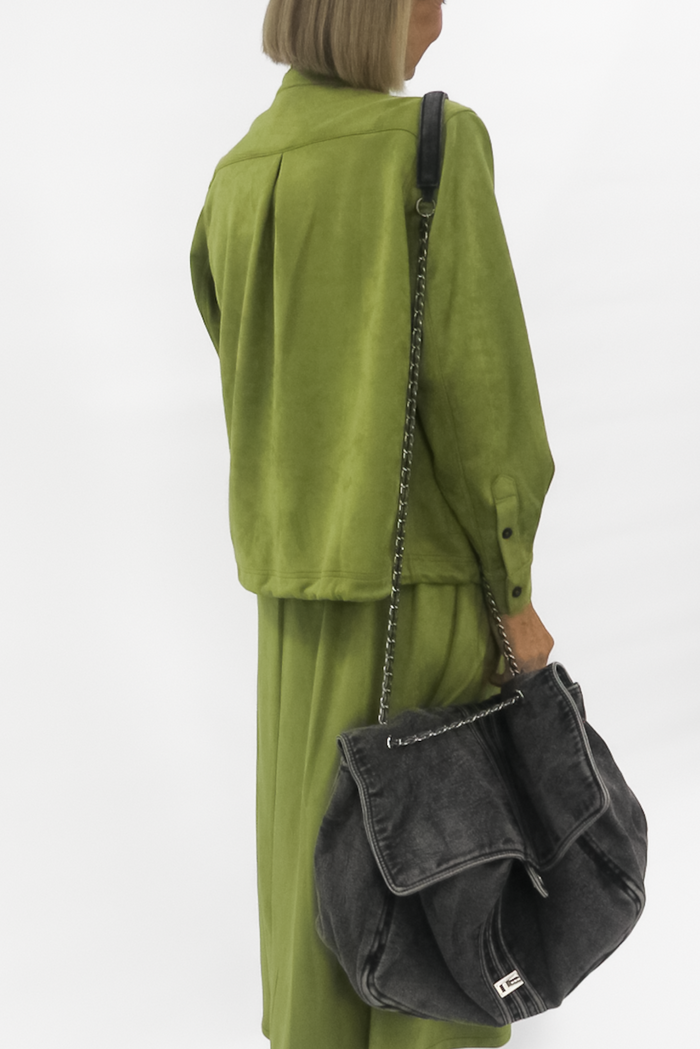 Person wearing a green vegan suede jacket  with a black bag on a white background