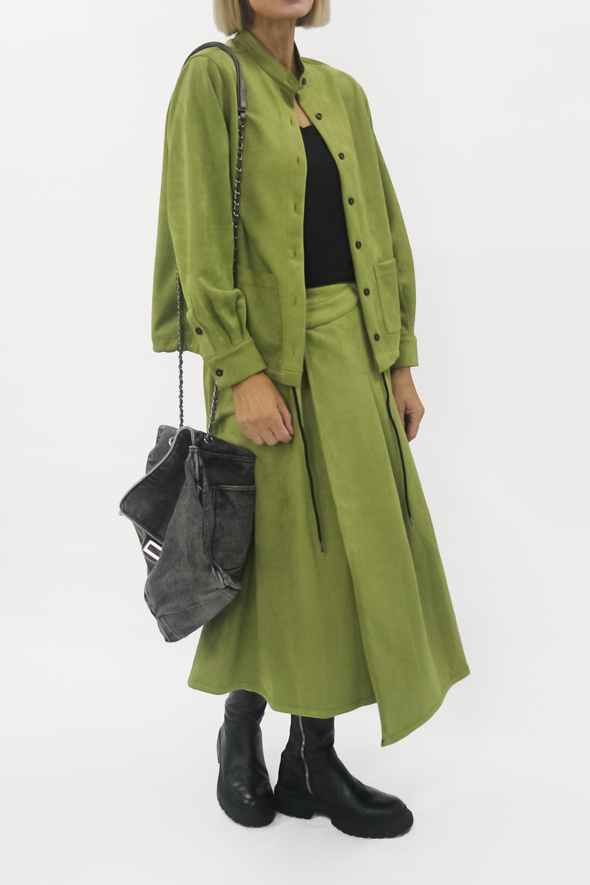 Person wearing a green skirt with a black top and holding a gray bag on a white background