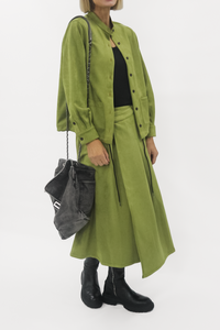 Person wearing a green skirt with a black top and holding a gray bag on a white background
