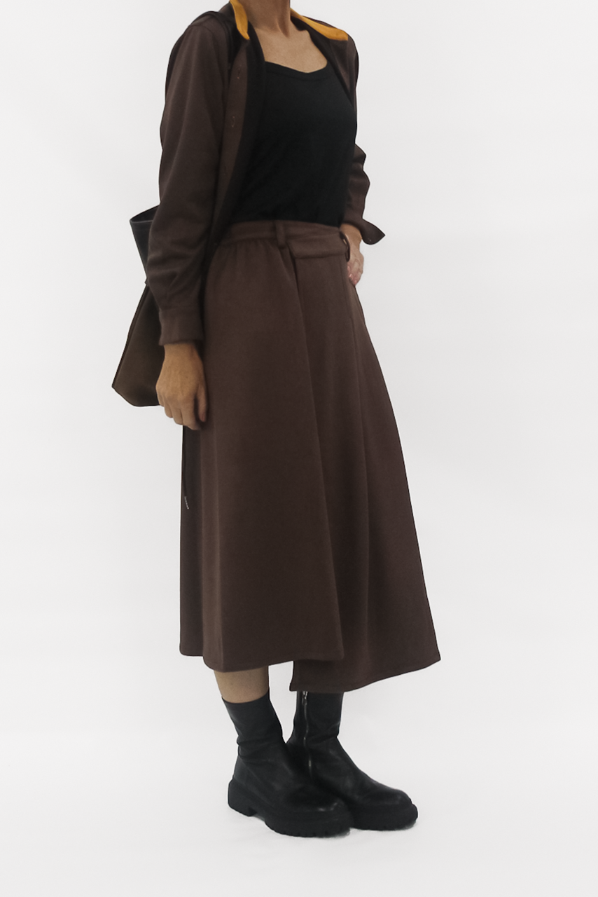 Person wearing a brown coat, black top, and skirt with black boots on a white background