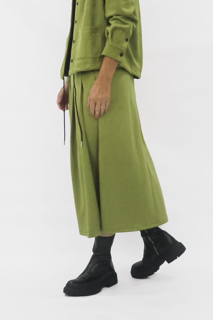 Person wearing a green skirt with a long skirt and black shoes on a white background