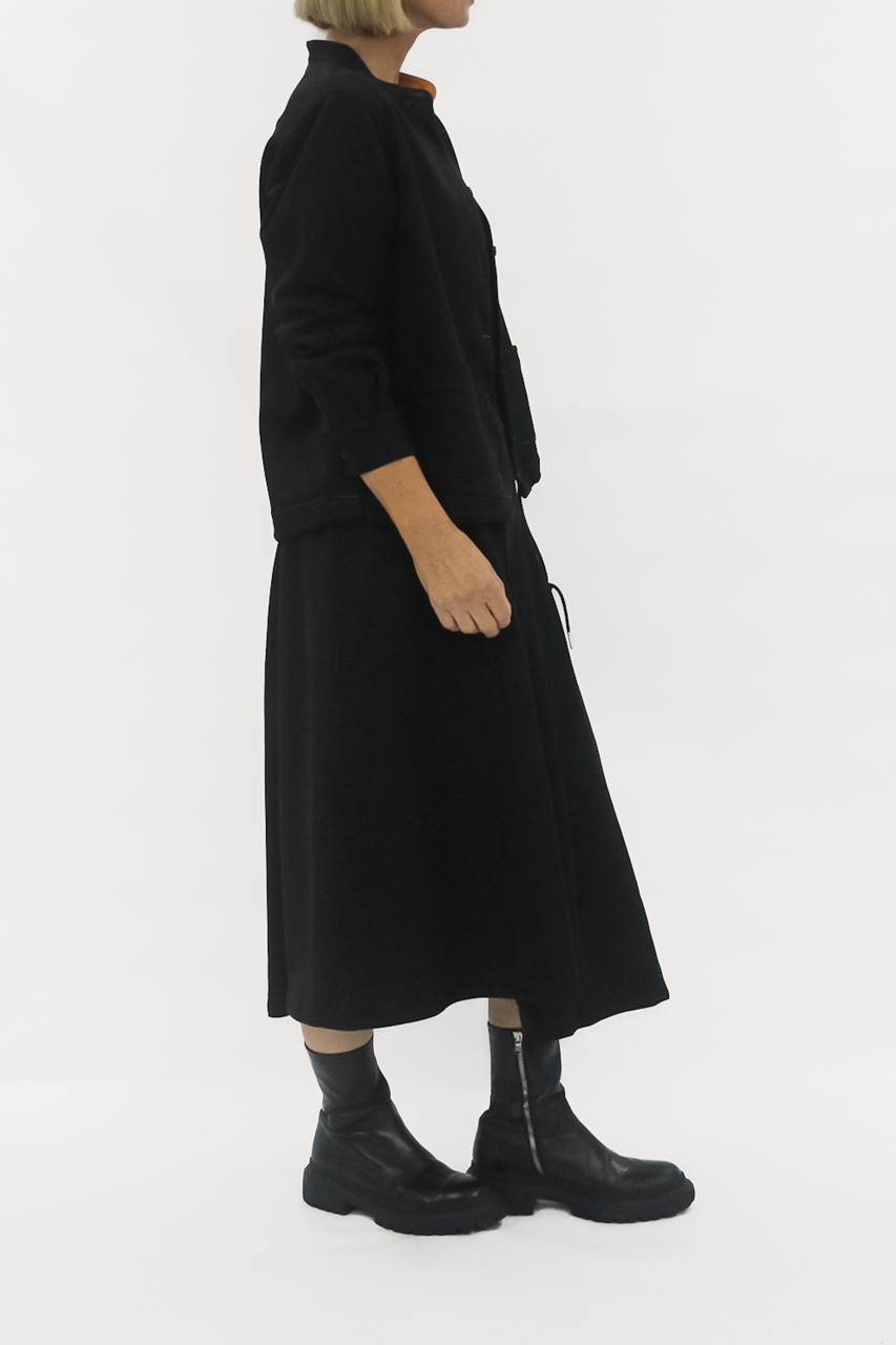 Person wearing a black outfit with a long dress and jacket on a white background